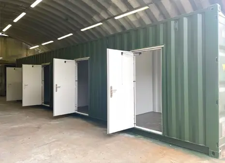 Green multi store container with multiple open personnel doors, positioned inside a paint booth.