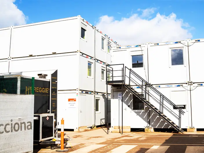 Stacked three-story modular building units connected with an external metal staircase on a construction site