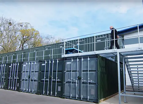 Multi store container unit installed above standard storage containers with secure access staircase and walkway at a self storage site in Great Britain.