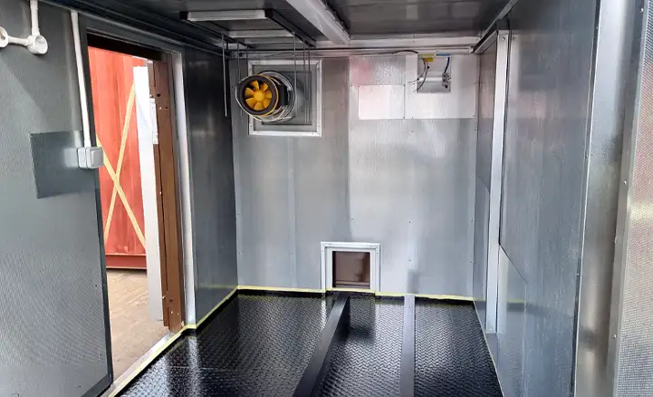 Interior of a containerised generator or compressor enclosure with sound-attenuated metal lining, ventilation fan, electrical fittings, and raised anti-slip flooring, designed for industrial equipment housing.