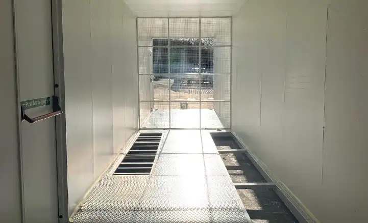 Interior of an empty converted shipping container by S Jones Containers, prepared for switchgear equipment installation. The space features a metal grated floor with recessed cable trays and a mesh security partition at the far end, allowing visibility while maintaining safety.