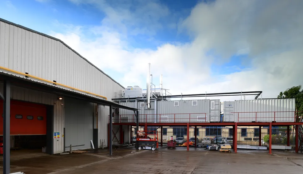 Elevated containerised boiler room installation at an industrial bakery site, with white containers mounted on a red steel platform alongside a large warehouse building.